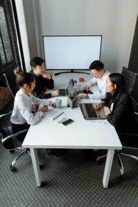 A group of professionals discussing a project in a modern office setting with laptops and a whiteboard.